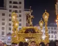 Procesi�n de un gran trono de Semana Santa avanzando por una calle del centro de M�laga rodeado de p�blico.