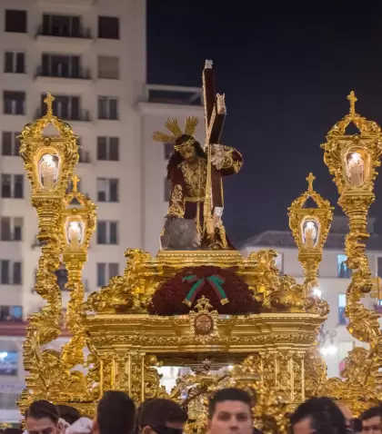 Procesi�n de un gran trono de Semana Santa avanzando por una calle del centro de M�laga rodeado de p�blico.