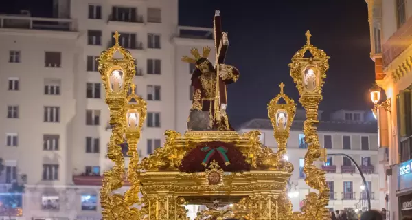 Procesi�n de un gran trono de Semana Santa avanzando por una calle del centro de M�laga rodeado de p�blico.