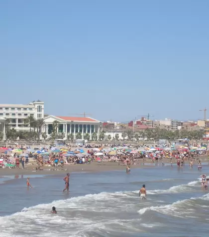 Playa urbana de Valencia en julio, con gente ba��ndose en el Mediterr�neo, agua tranquila, arena clara, sombrillas y ambiente c�lido.
